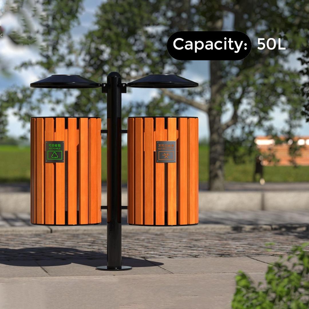 Two orange trash bins with a black pole in a park setting, labeled 'Capacity: 50L'.