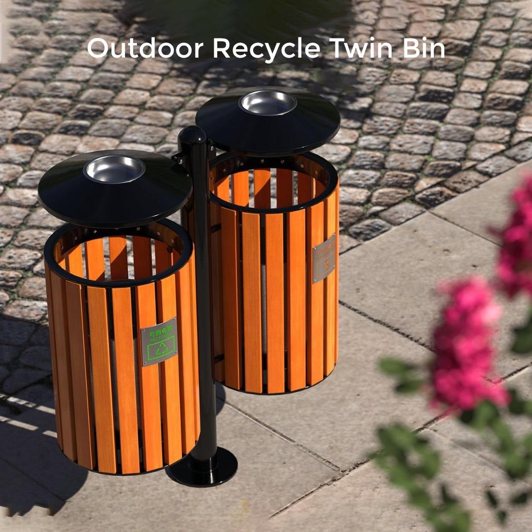 Outdoor recycle twin bin with orange cylindrical design on a paved surface.